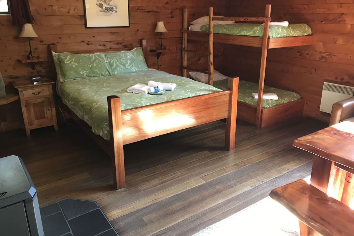 Habitación con literas de madera, colcha verde, mesita de noche con lámpara y un cuadro enmarcado en la pared.