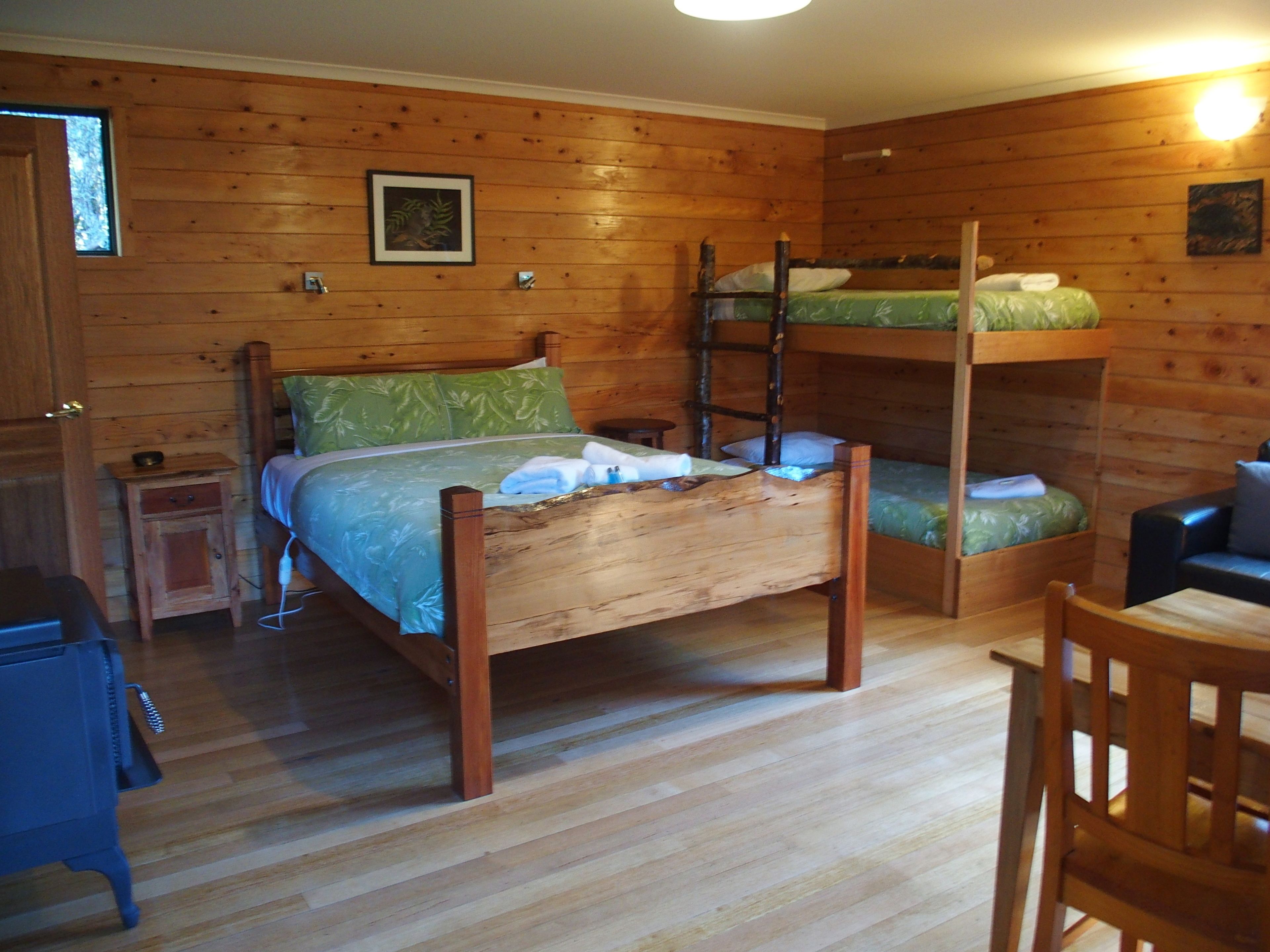 Quarto em estilo cabana de madeira com beliches, uma pequena mesa de cabeceira e uma cadeira.