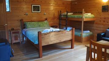 Quarto em estilo cabana de madeira com beliches, uma pequena mesa de cabeceira e uma cadeira.