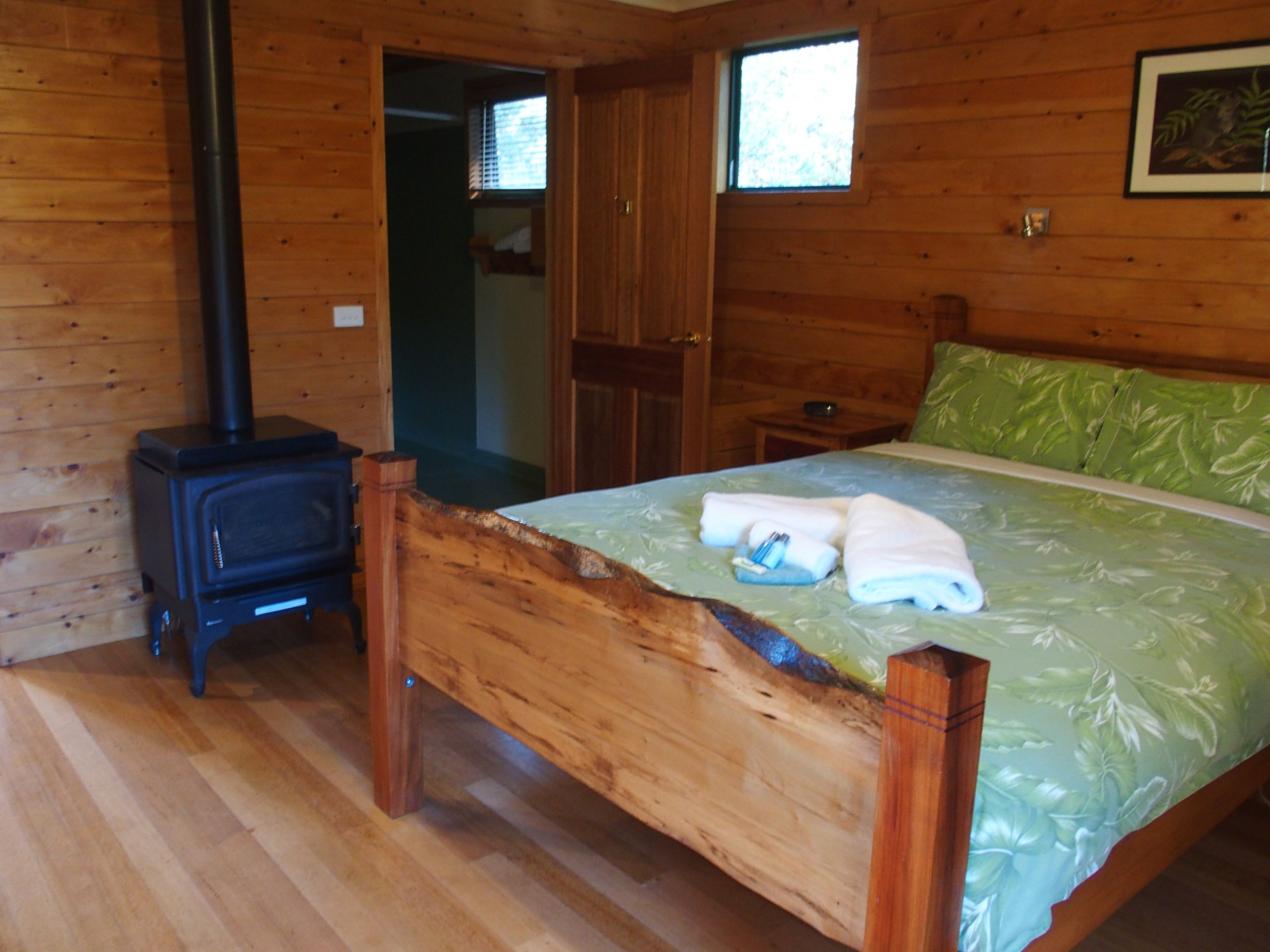 Une pièce de cabane en bois comprenant un lit, un plancher en bois, une fenêtre et un poêle à bois.