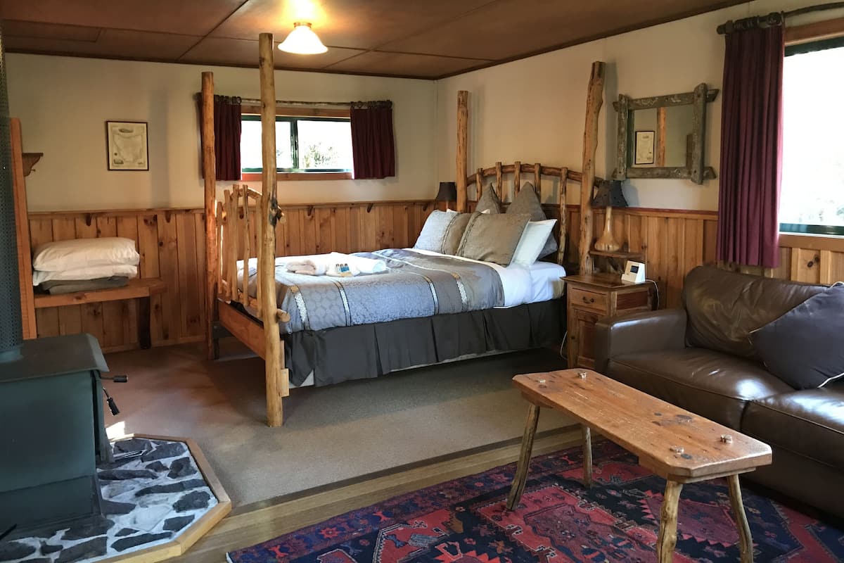 Una habitación rústica con una cama con dosel de madera, un sofá de cuero, una mesita de madera pequeña y una alfombra estampada.