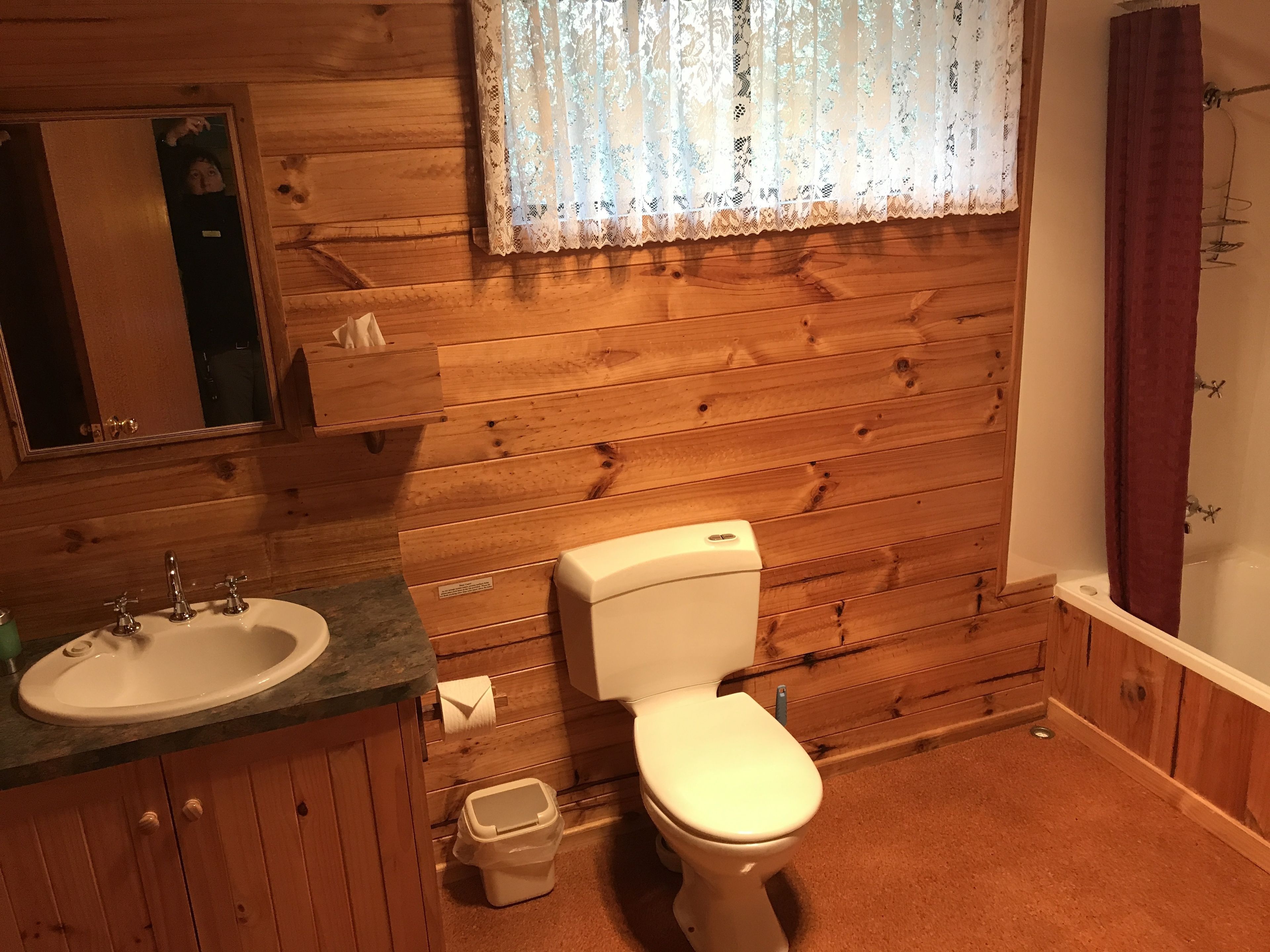 Ein Badezimmer mit Holzvertäfelung, Waschbecken, Toilette und Spiegel.