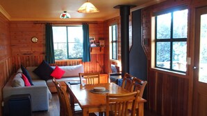 A cozy cabin interior with a wooden dining table, chairs, a sofa, and a fireplace. - Cradle Highlander (Cradle Mountain)