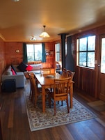 Un interior acogedor de cabaña con una mesa de comedor de madera, sillas, un sofá y una chimenea.