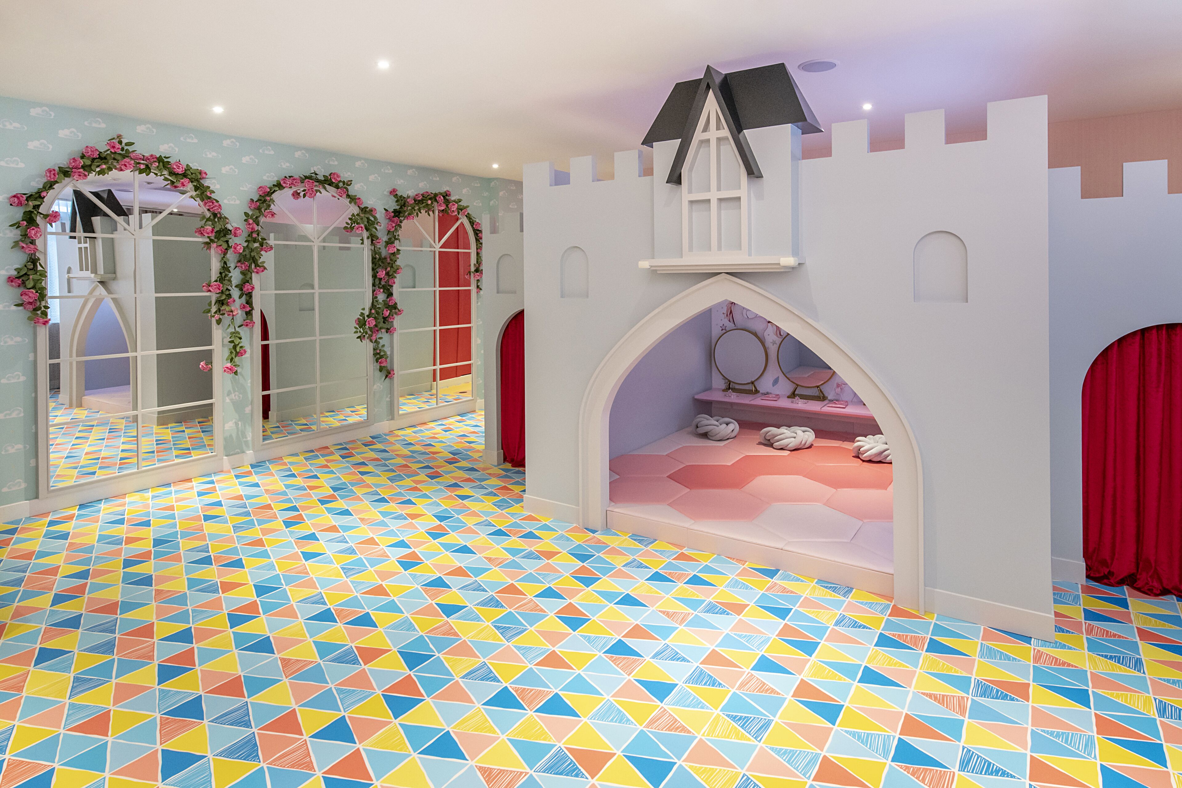 Een speelkamer met een kleurrijk geometrisch vloerpatroon, spiegelwanden en een speelhuisje in kasteelthema met een raam en rode gordijnen.