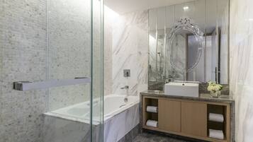 A modern bathroom with a glass-enclosed shower, a marble-tiled wall, a large mirror, and a wooden vanity with a sink and towel racks.