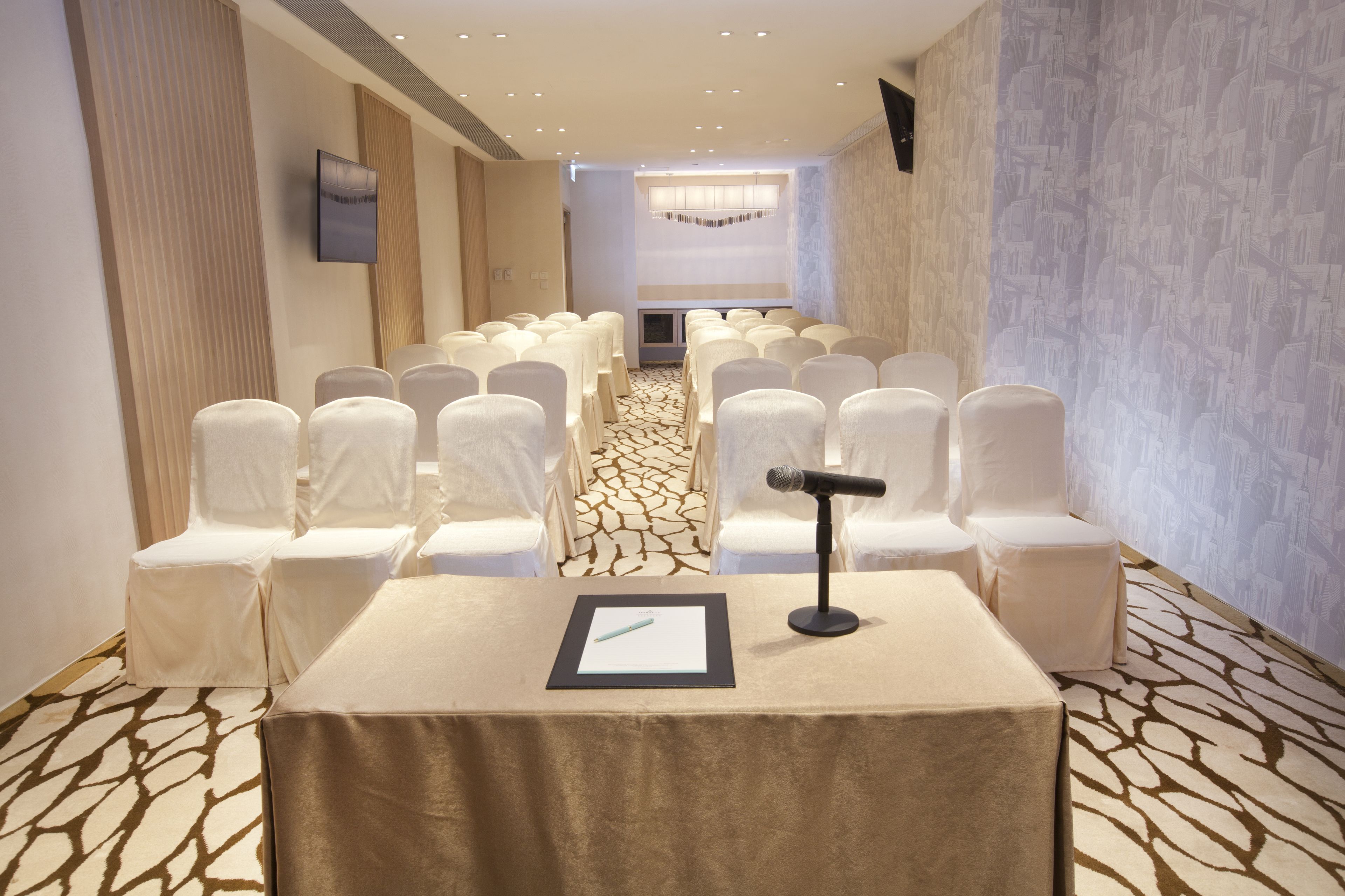 Un salón de conferencias con filas de sillas blancas, un atril y suelo alfombrado.