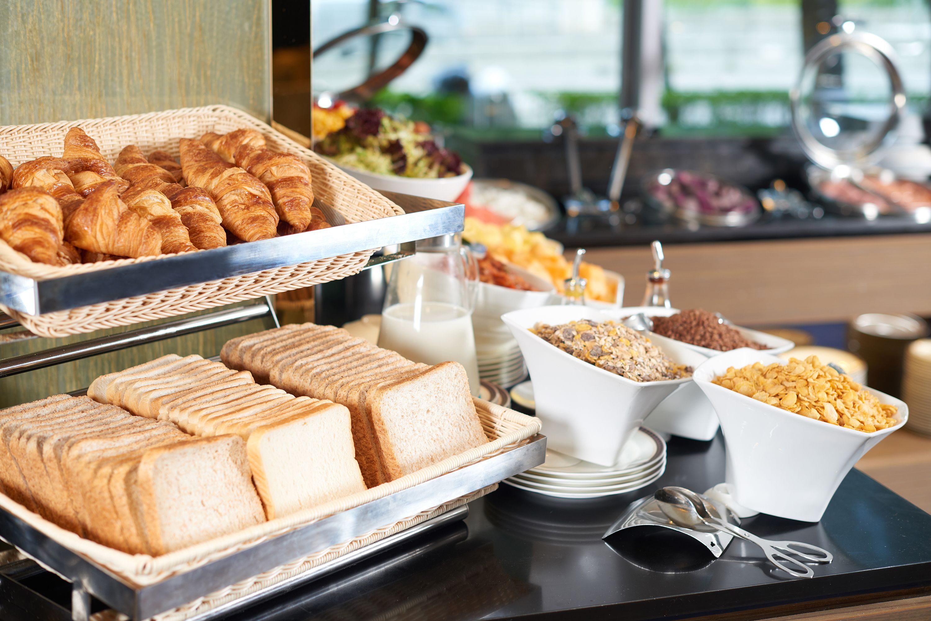 A buffet with bread, croissants, and cereal.