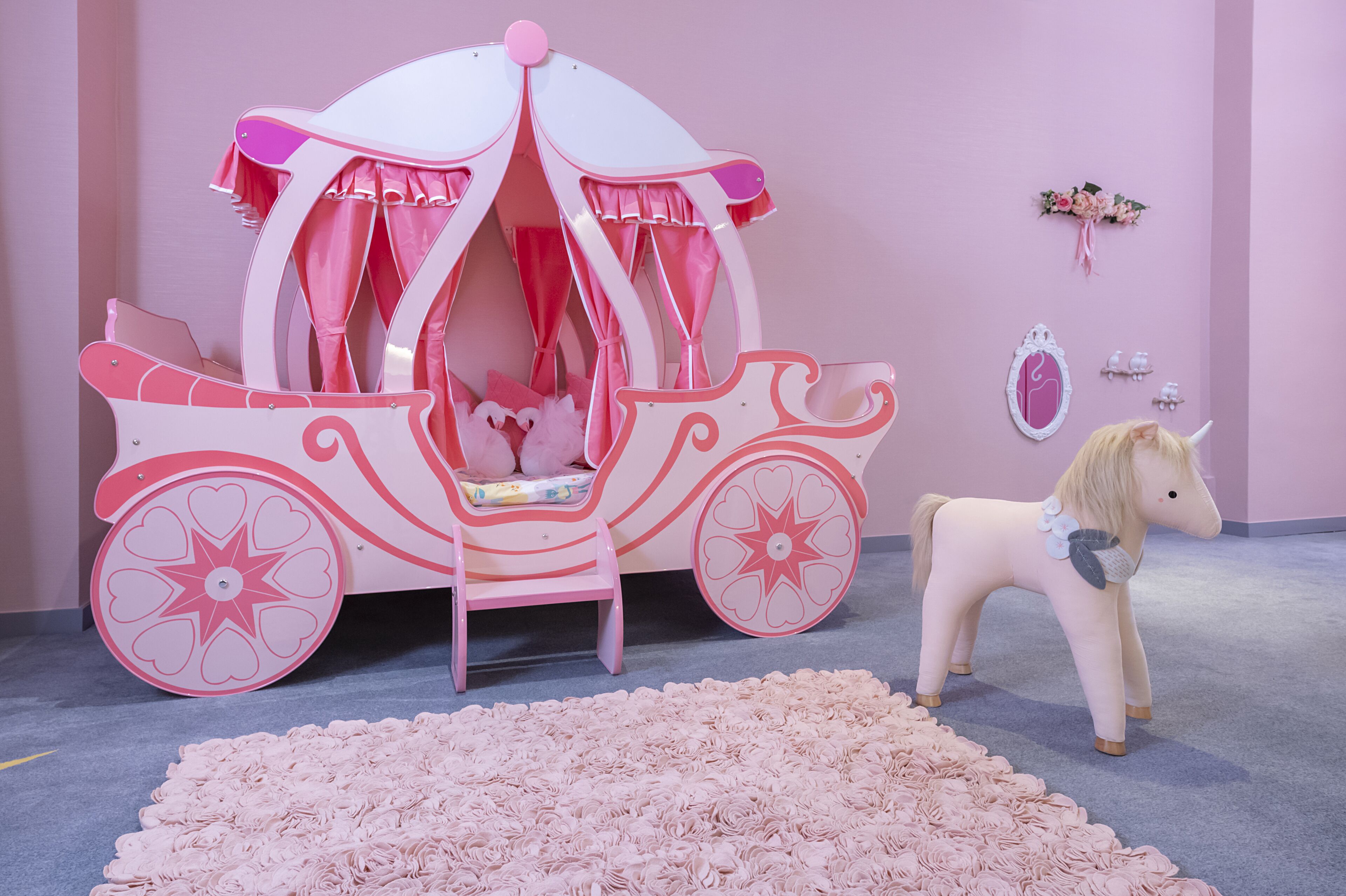 Una habitación con temática rosa, con un carruaje decorativo y un caballo de juguete.