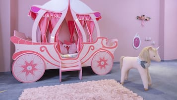Una habitación con temática rosa, con un carruaje decorativo y un caballo de juguete.