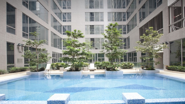 Una piscina interior moderna con agua azul cristalina, rodeada por un solárium con baldosas y un edificio de varios pisos con amplios ventanales.