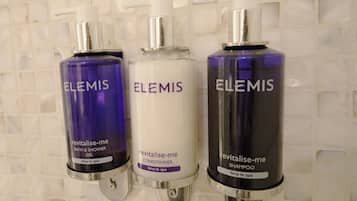 Tres botellas de productos Elemis sobre una pared de azulejos.