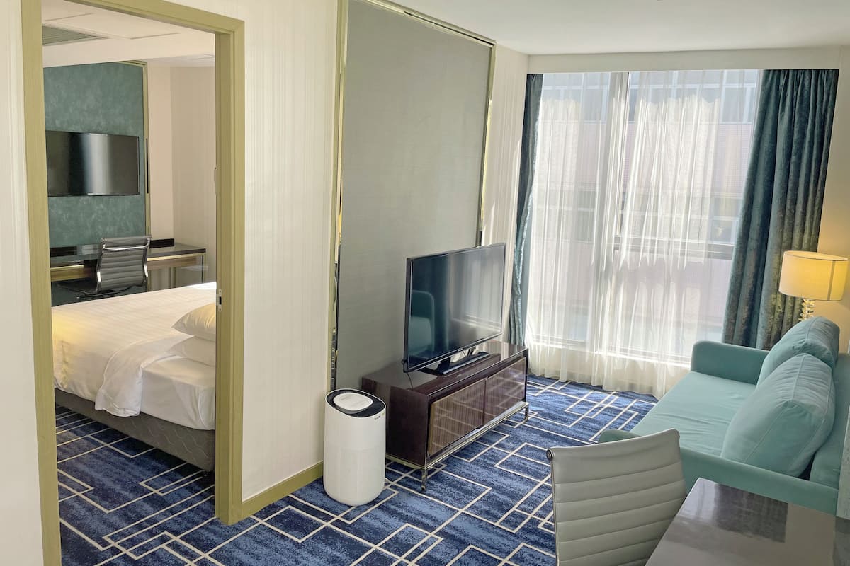 Et hotelværelse med en seng, et fjernsyn, et skrivebord med stol, en sofa og en lampe.