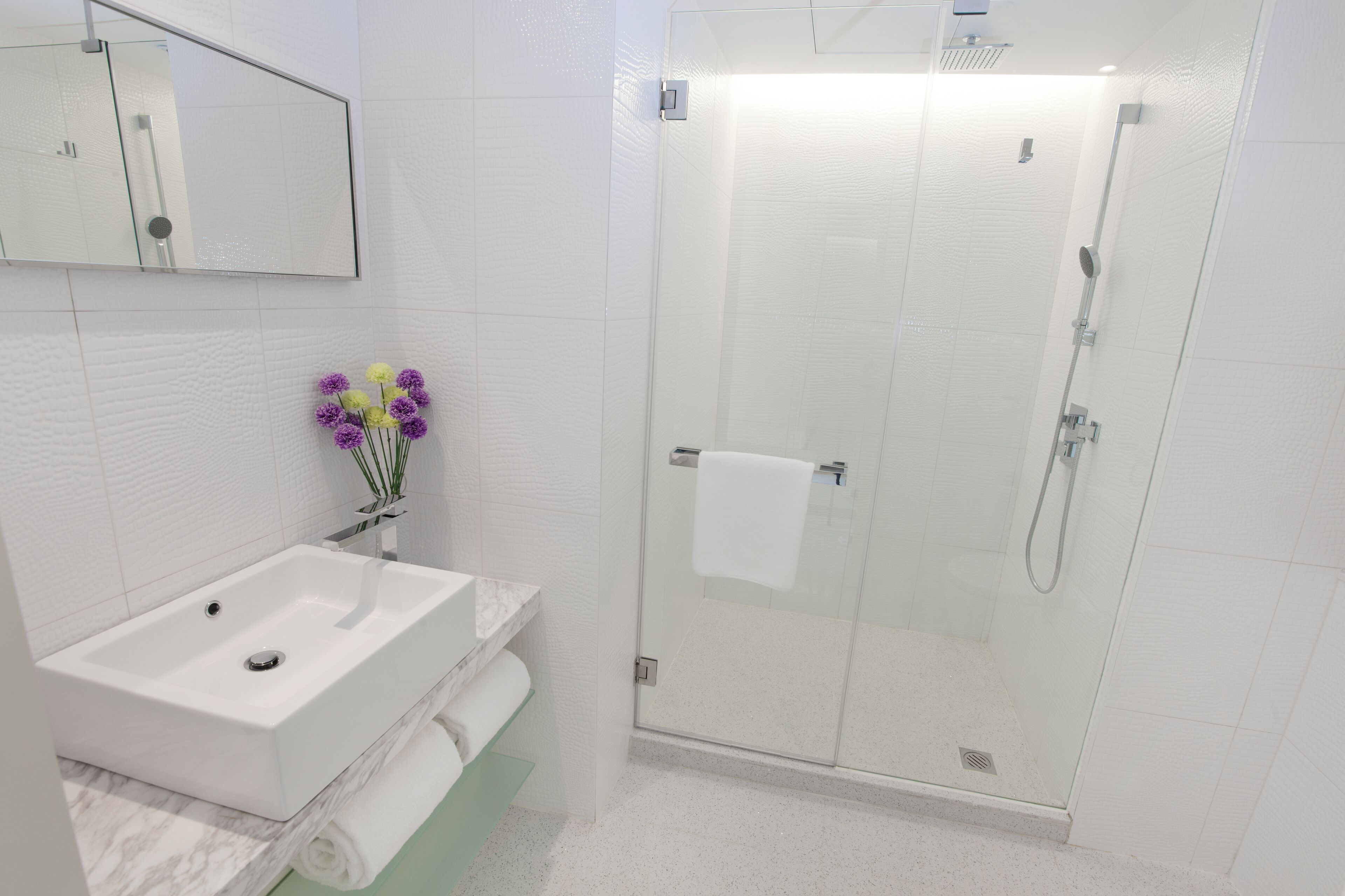 A modern bathroom with a white sink, mirror, and glass shower enclosure.