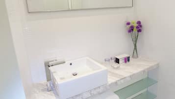 A bathroom with a white sink, a mirror above it, and a vase with purple flowers on the counter.