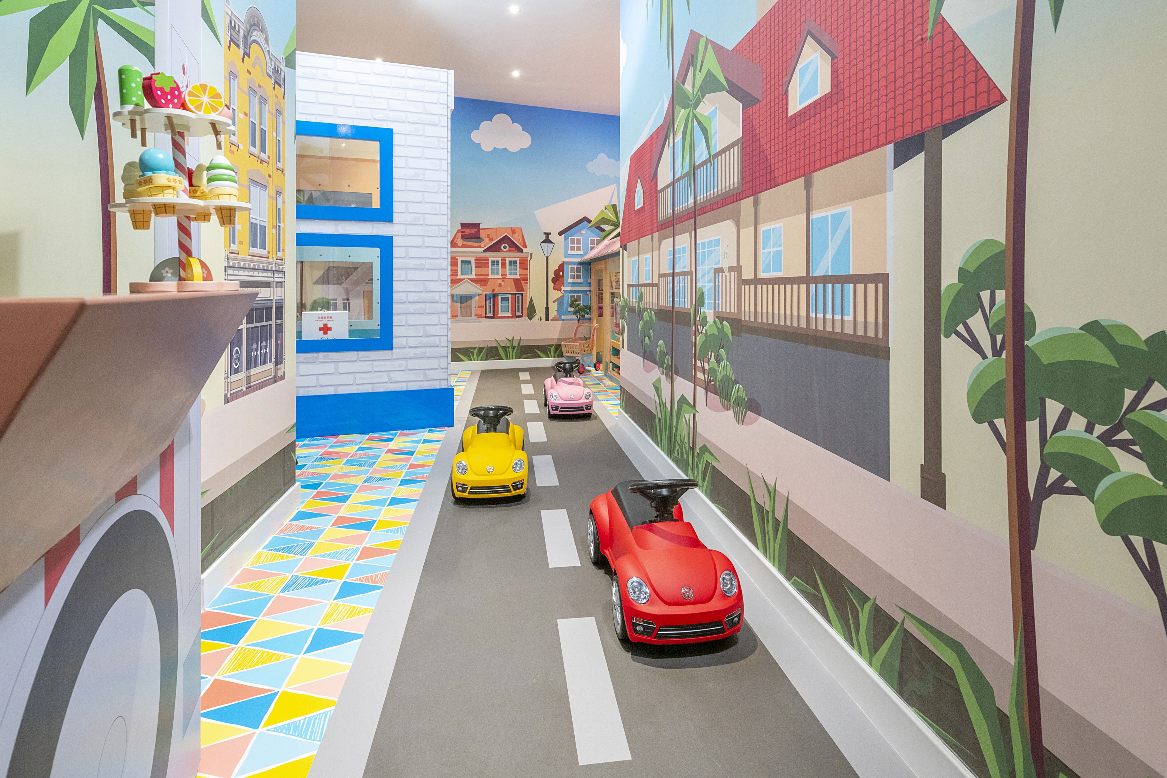 Zona de juegos infantiles con coches de colores y un mural de casas.