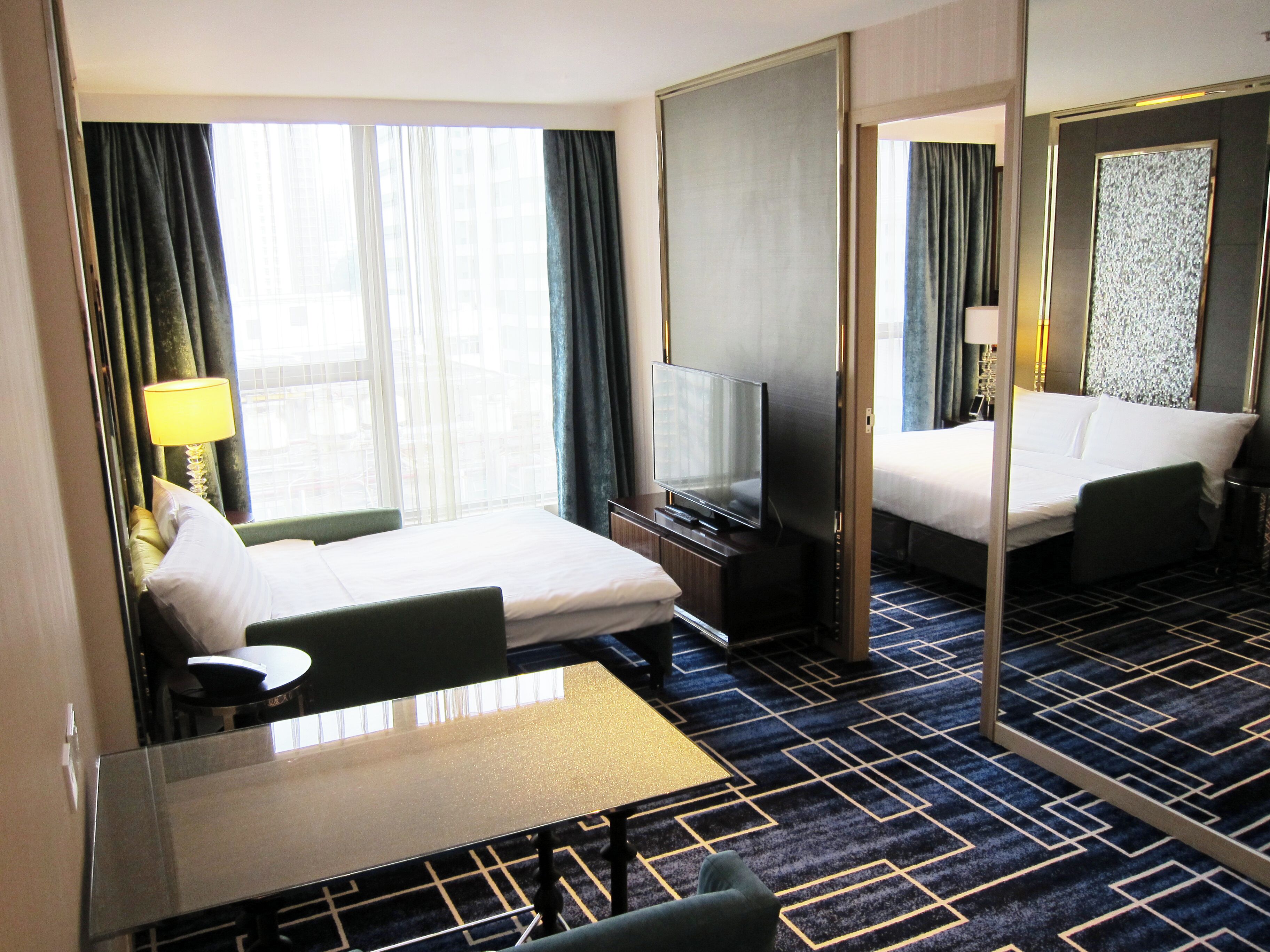 A hotel room with a bed, a desk, a television, and a large mirror.