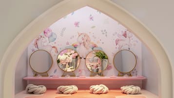A room with a pink vanity, three round mirrors, and a floral mural on the wall.