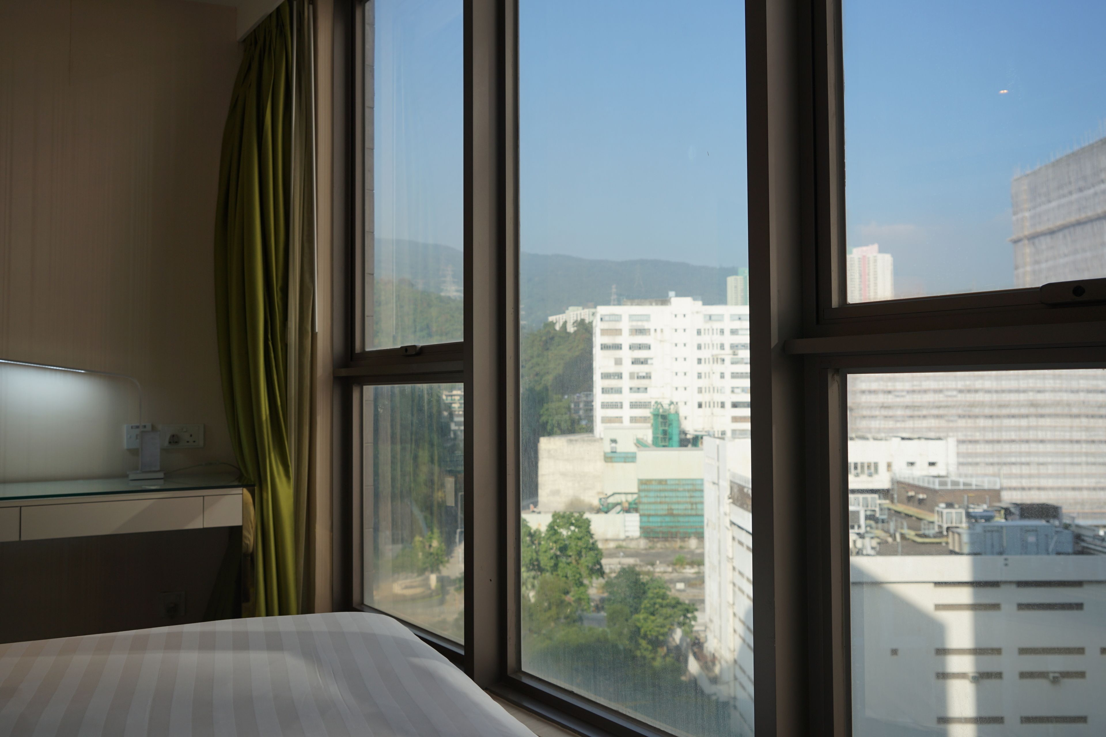 A hotel room with a large window, a bed, a desk, and a green curtain.