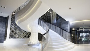 Una escalera en espiral moderna con barandilla metálica, rodeada por un suelo pulido y un diseño geométrico en la pared.