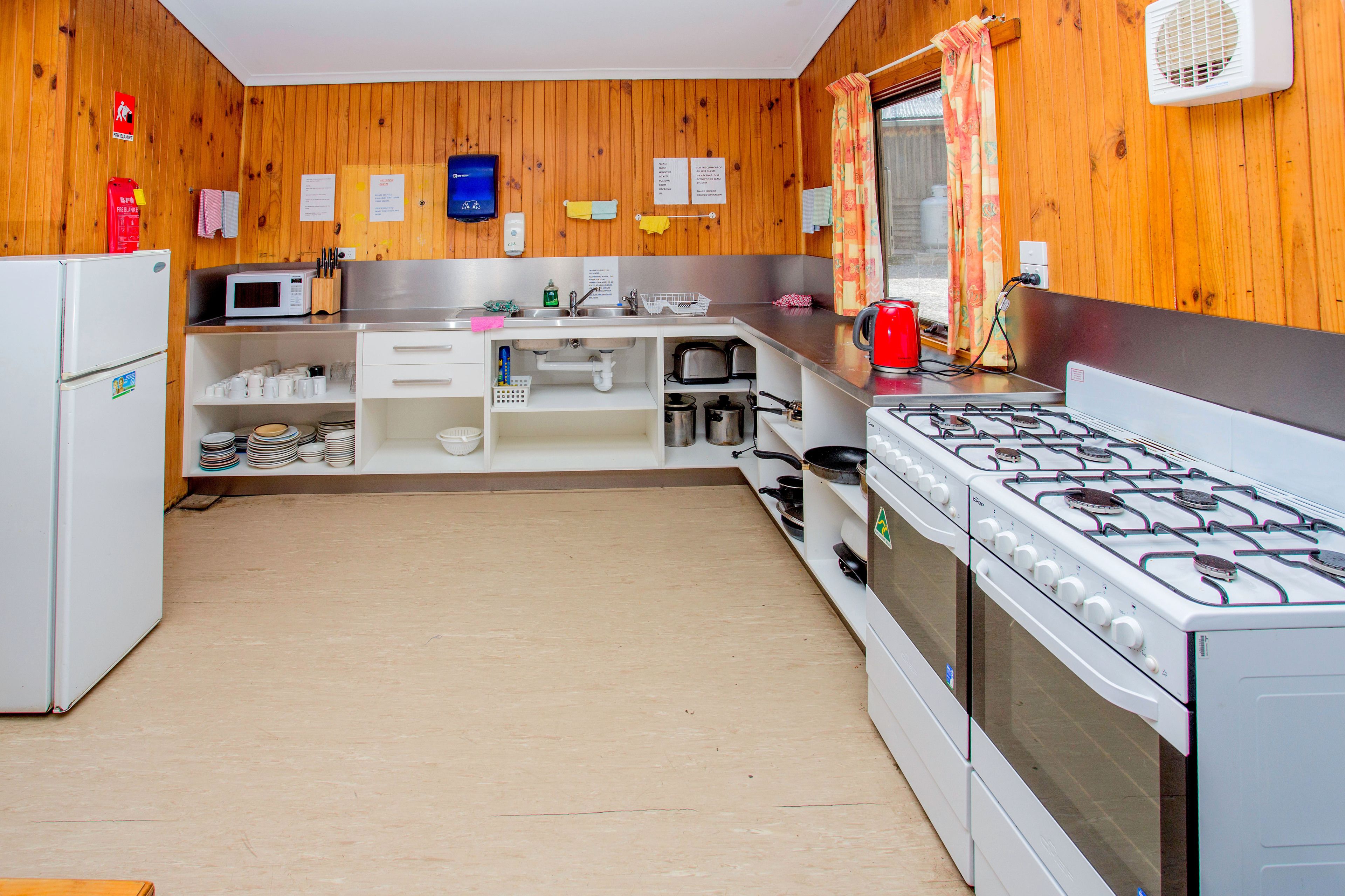 A kitchen with wooden walls, white cabinets, a gas stove, a microwave, and a refrigerator.