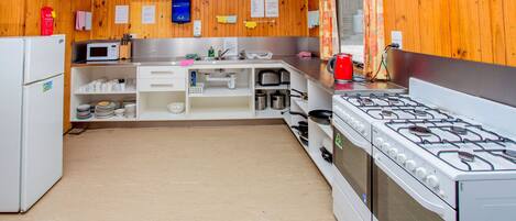 Una cocina con paredes de madera, armarios blancos, estufa a gas, microondas y refrigerador.