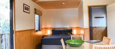 A compact bedroom with a bed, bedside lamps, a small table with a green bowl, and a door.