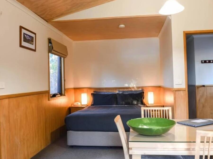 A compact bedroom with a bed, bedside lamps, a small table with a green bowl, and a door.