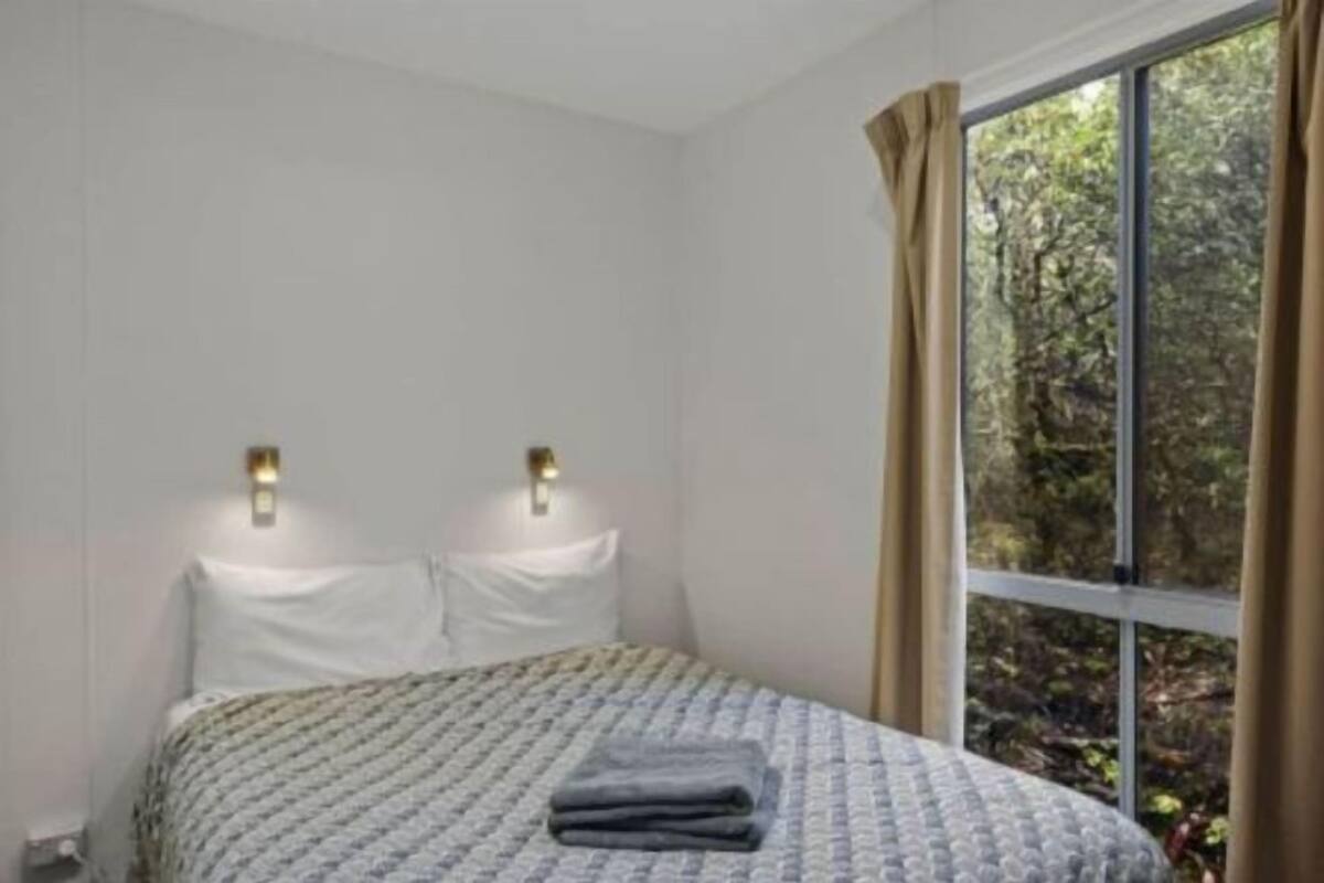 A bedroom with a bed, two wall-mounted lights, a window with curtains, and a view of trees.