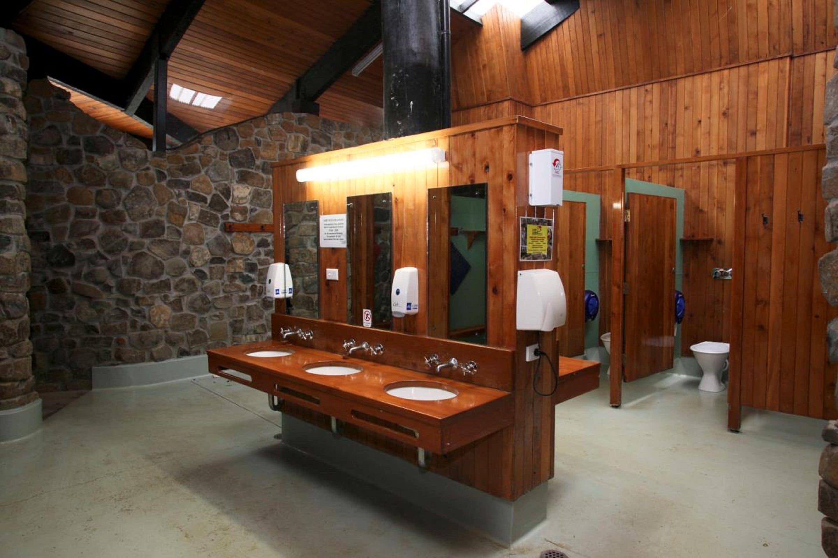 Un baño de madera con tres lavamanos, un espejo y un secador de manos.