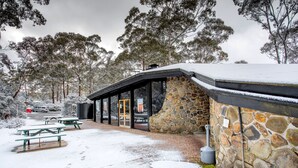 Un edificio de piedra con un patio cubierto, mesas de picnic y un muro de piedra.