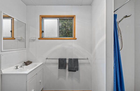 A bathroom with a white sink, mirror, and window. There is a towel rack with two towels and a shower curtain. - Discovery Parks - Cradle Mountain (Cradle Mountain)