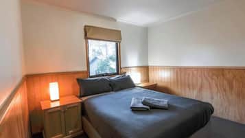Une chambre à coucher avec un lit, une table de chevet, une fenêtre donnant sur un beau paysage et des lambris en bois sur les murs.