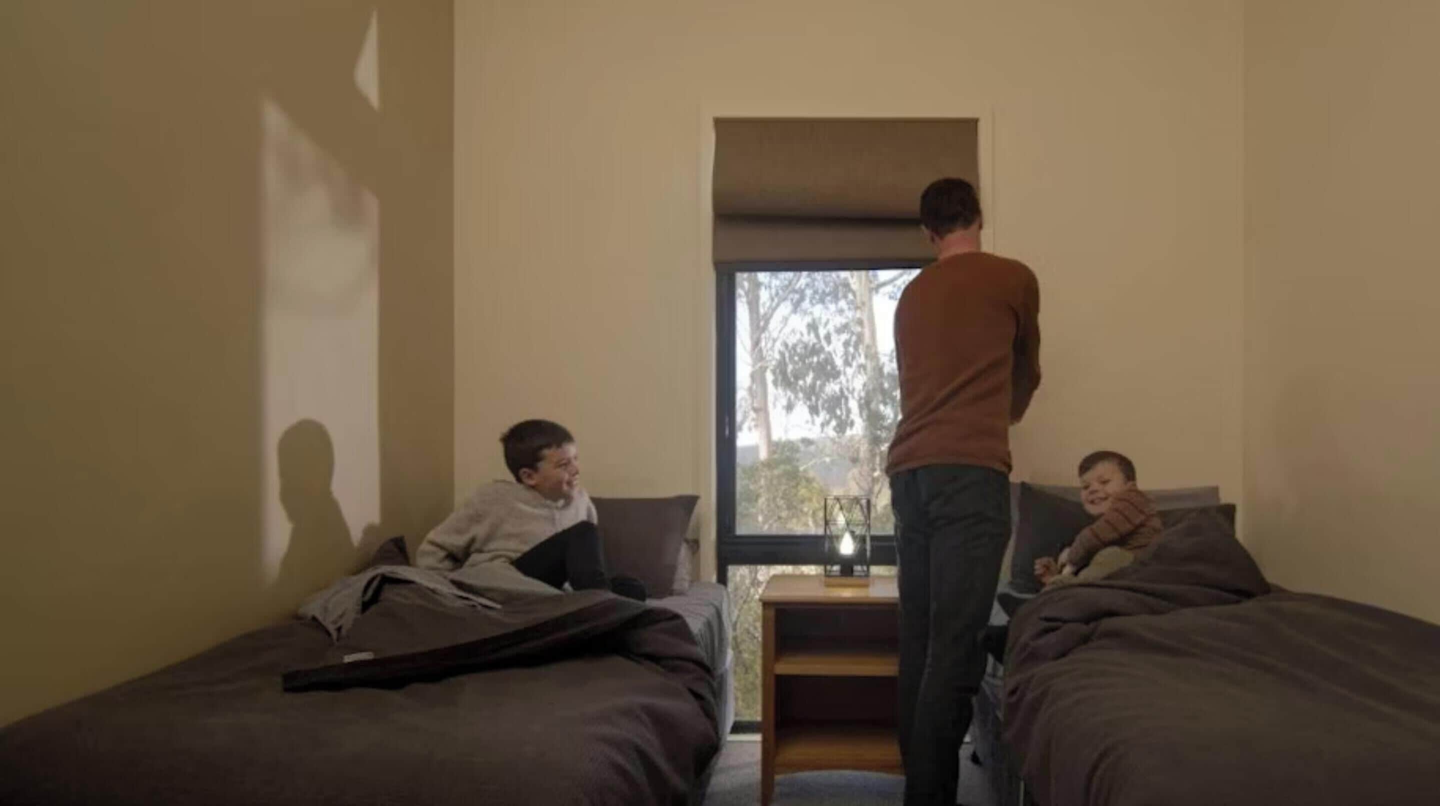 A room with two beds, a nightstand, and a window.