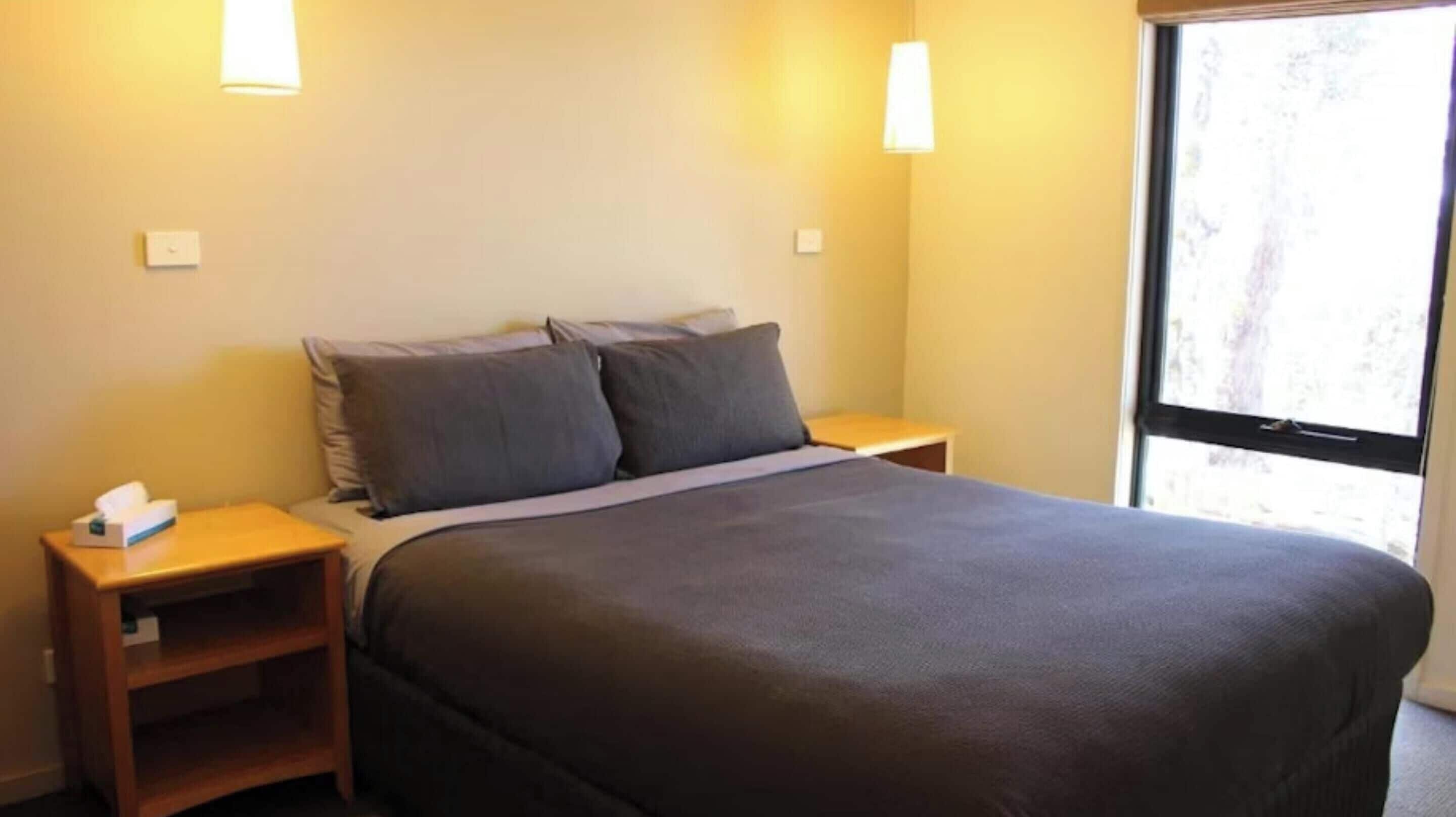Un dormitorio con una cama, dos mesitas de noche y una ventana.