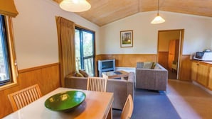 Una habitación acogedora con una mesa de comedor, un bol verde, dos sofás, un televisor y una zona de cocina.