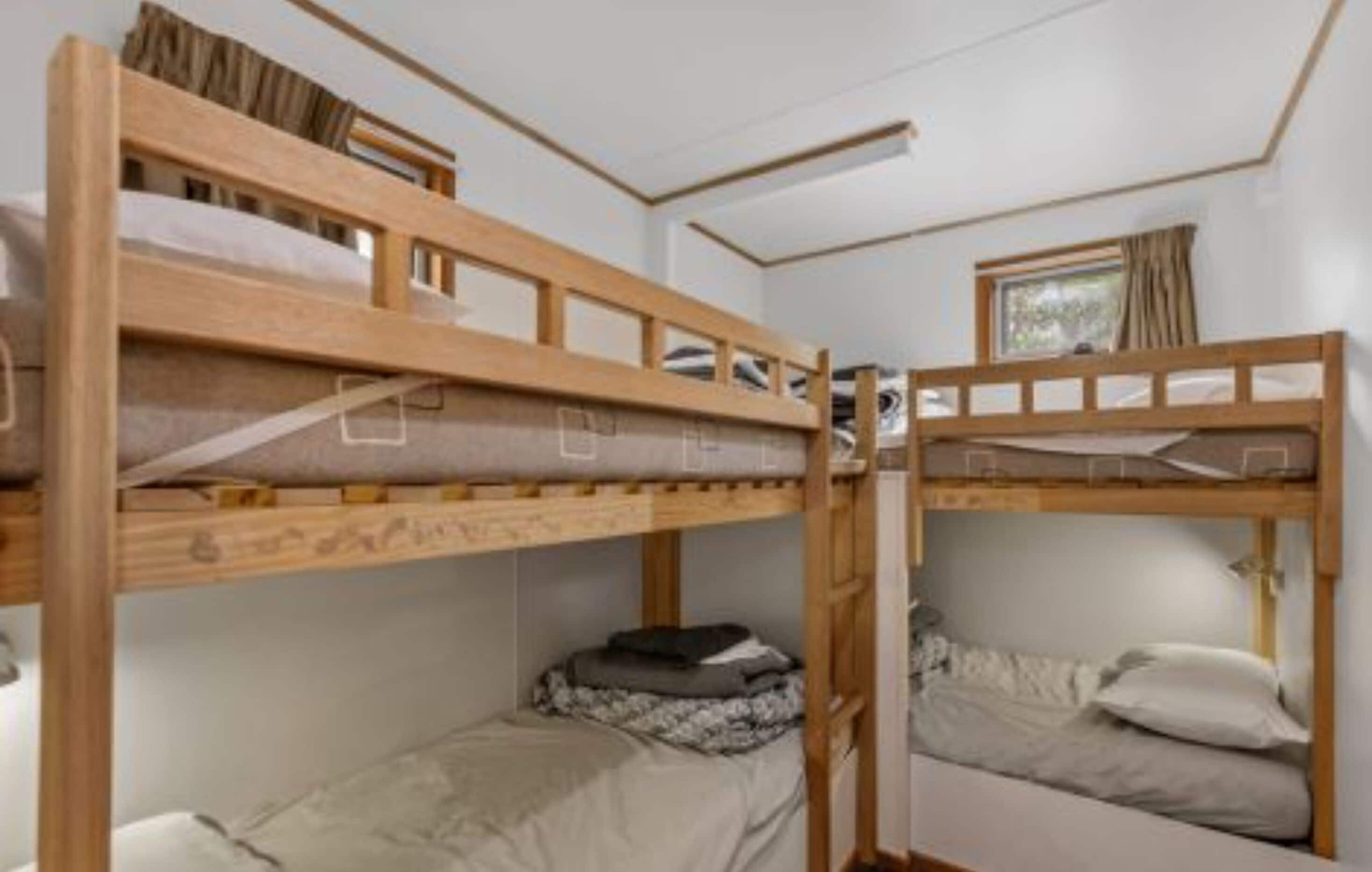 Una habitación con dos literas, una ventana con cortinas y una mesita pequeña.
