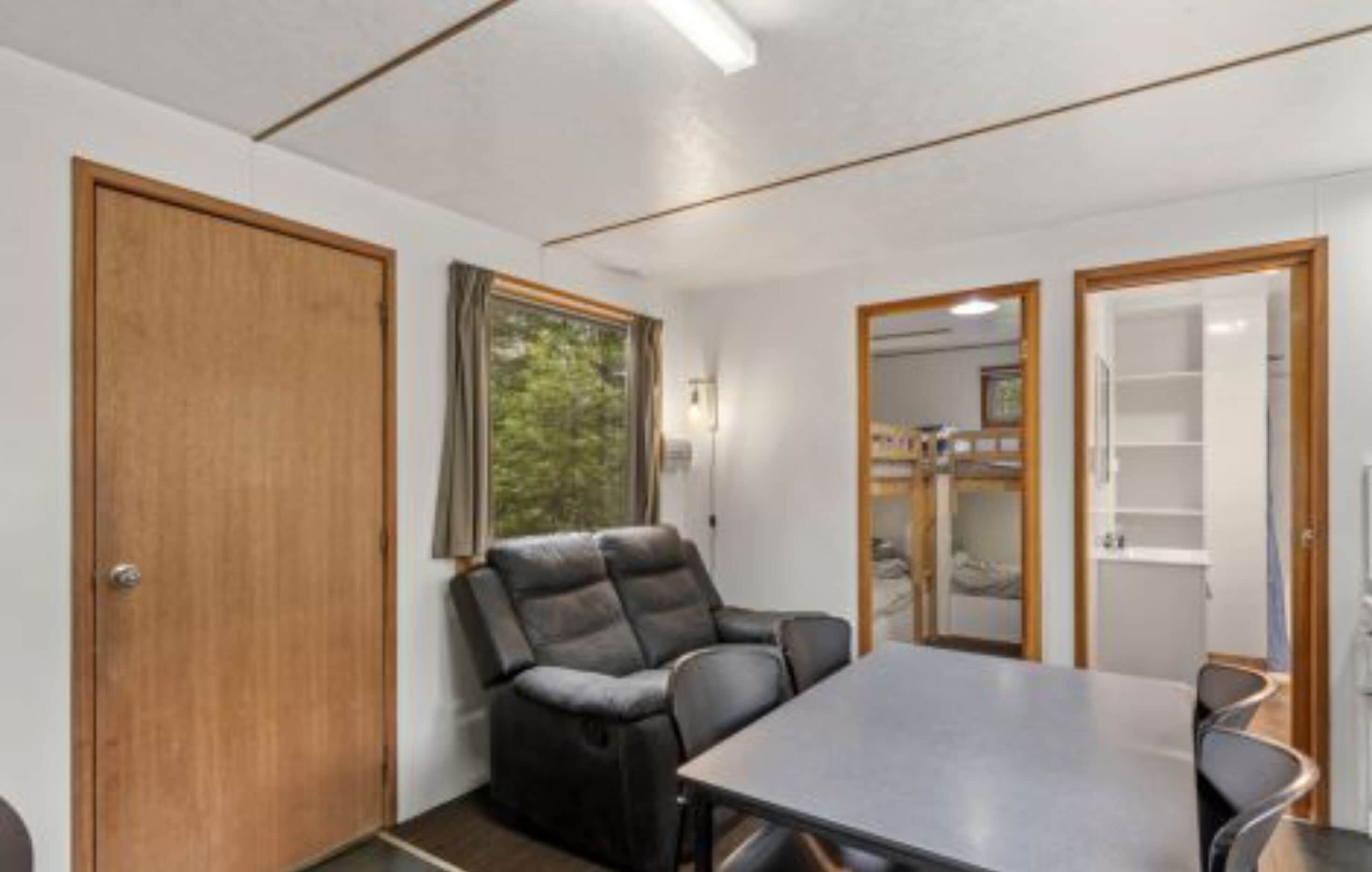 A room with a wooden door, a window, a sofa, a table, and a shelving unit.
