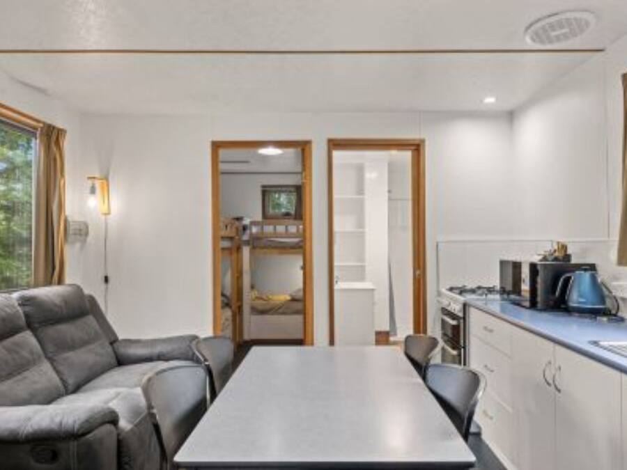 Een compacte kamer met een bank, een eettafel, een kitchenette en uitzicht op een tuin.