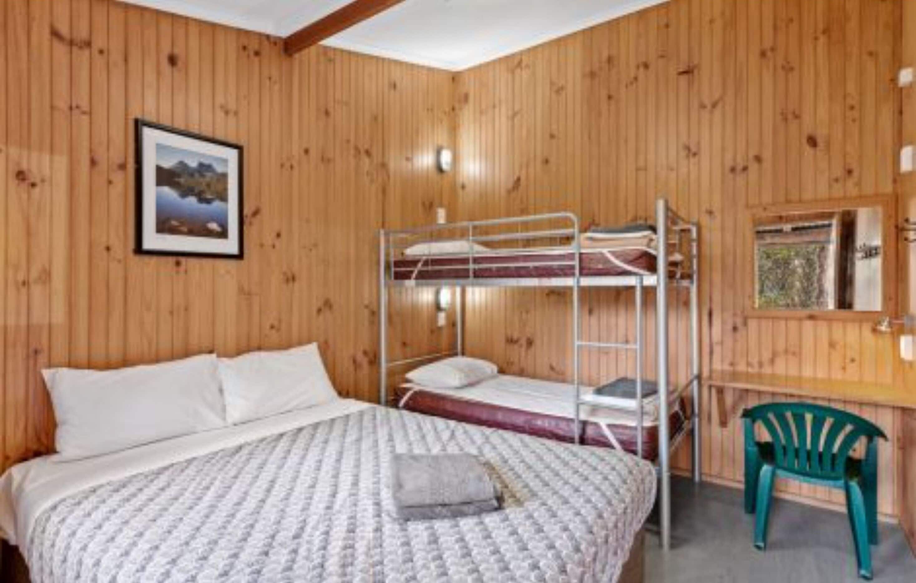 A wooden-paneled room with bunk beds, a desk, and a chair.