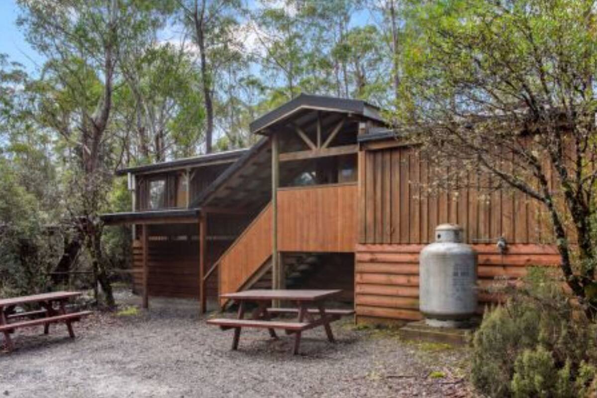 A rustic cabin with a wooden exterior, a staircase leading to an upper level, and a propane tank nearby.