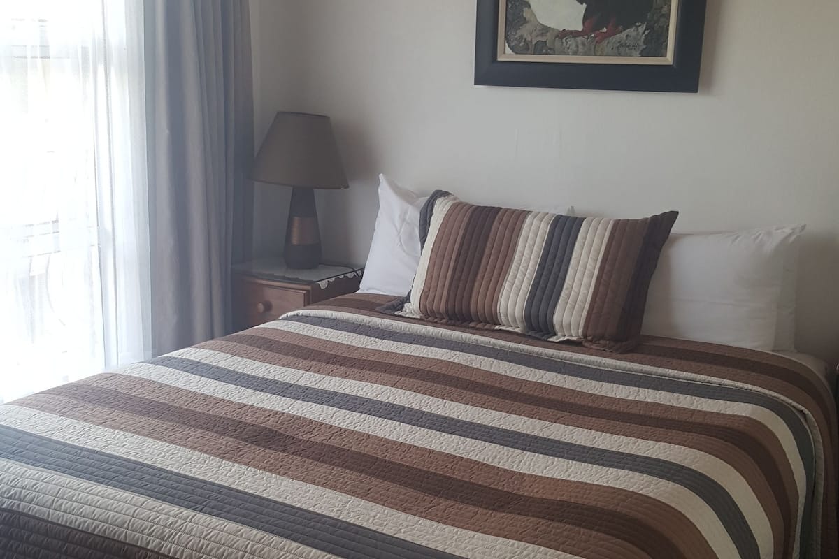 A bedroom with a large bed, a nightstand, a lamp, and a framed picture on the wall.