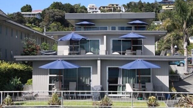 A modern two-story building with large windows and outdoor seating areas with umbrellas. - Bayview Motel (Paihia)