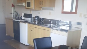 A compact kitchen with wooden cabinets, a microwave, a coffee maker, and a sink. There is a dining table with four chairs. - Bayview Motel (Paihia)