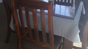 A dining area with a table and four wooden chairs, a flat-screen TV mounted on the wall, and a window with curtains. - Bayview Motel (Paihia)