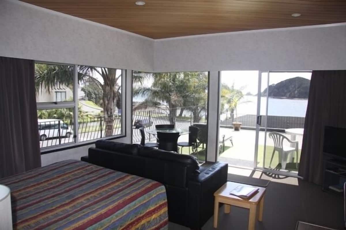 A hotel room with a large bed, a black leather sofa, a small table, and a view of the sea through large windows.