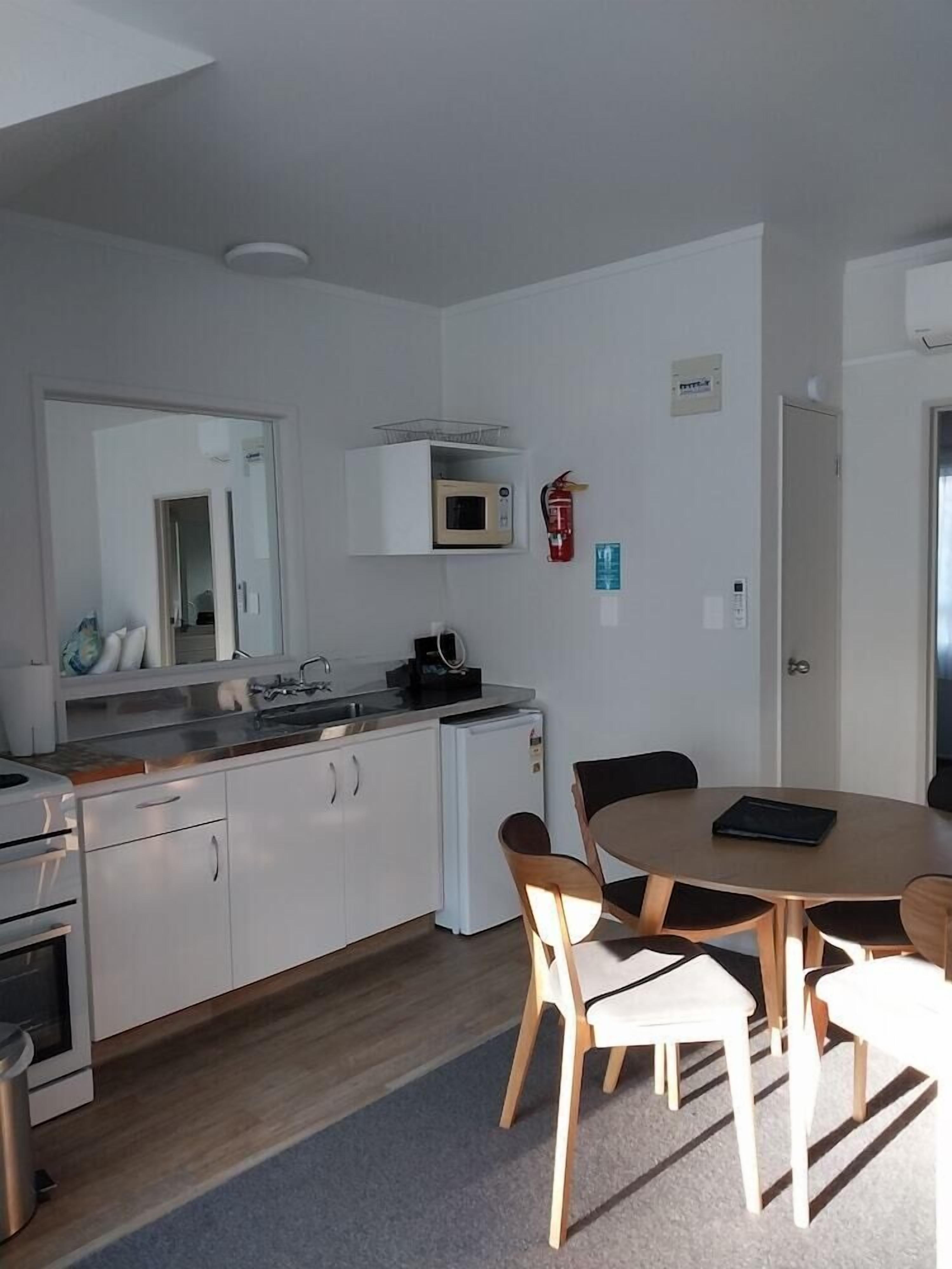 Eine kompakte Küche mit weißen Schränken, einer Mikrowelle und einer Kaffeemaschine. Es gibt einen Esstisch mit Stühlen und einen kleinen Kühlschrank.