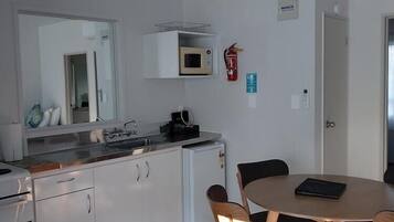Eine kompakte Küche mit weißen Schränken, einer Mikrowelle und einer Kaffeemaschine. Es gibt einen Esstisch mit Stühlen und einen kleinen Kühlschrank.