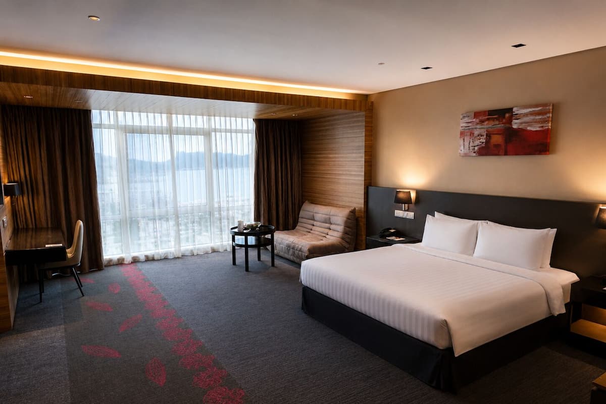 A hotel room with a large bed, a desk, a chair, a small table, and a large window with curtains.