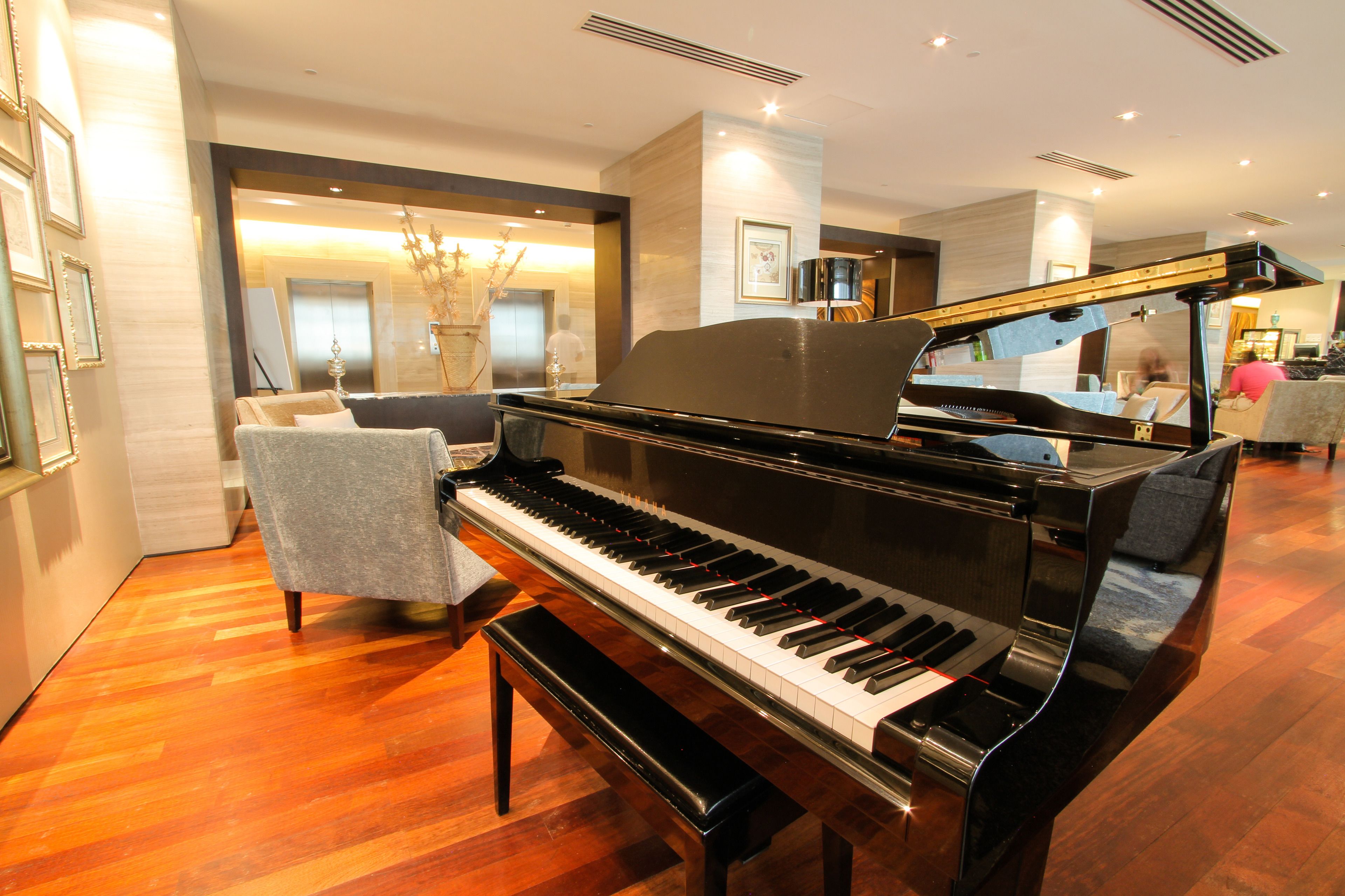 Un piano de cola en una habitación luminosa con suelo de madera, un taburete y una zona de estar con una silla.